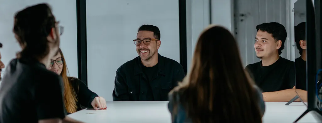 Time da Prod reunido em volta de uma mesa, sorrindo durante conversa de projeto.
