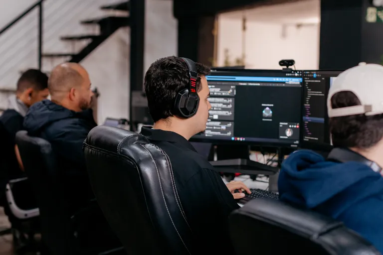 Pessoa do time da Prod trabalhando em múltiplos monitores, de costas, no escritório.
